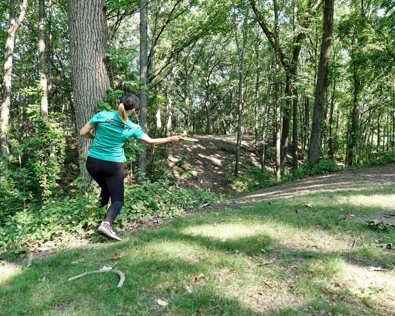Professional disc golf throwing a forehand throw in a wooded disc golf course.